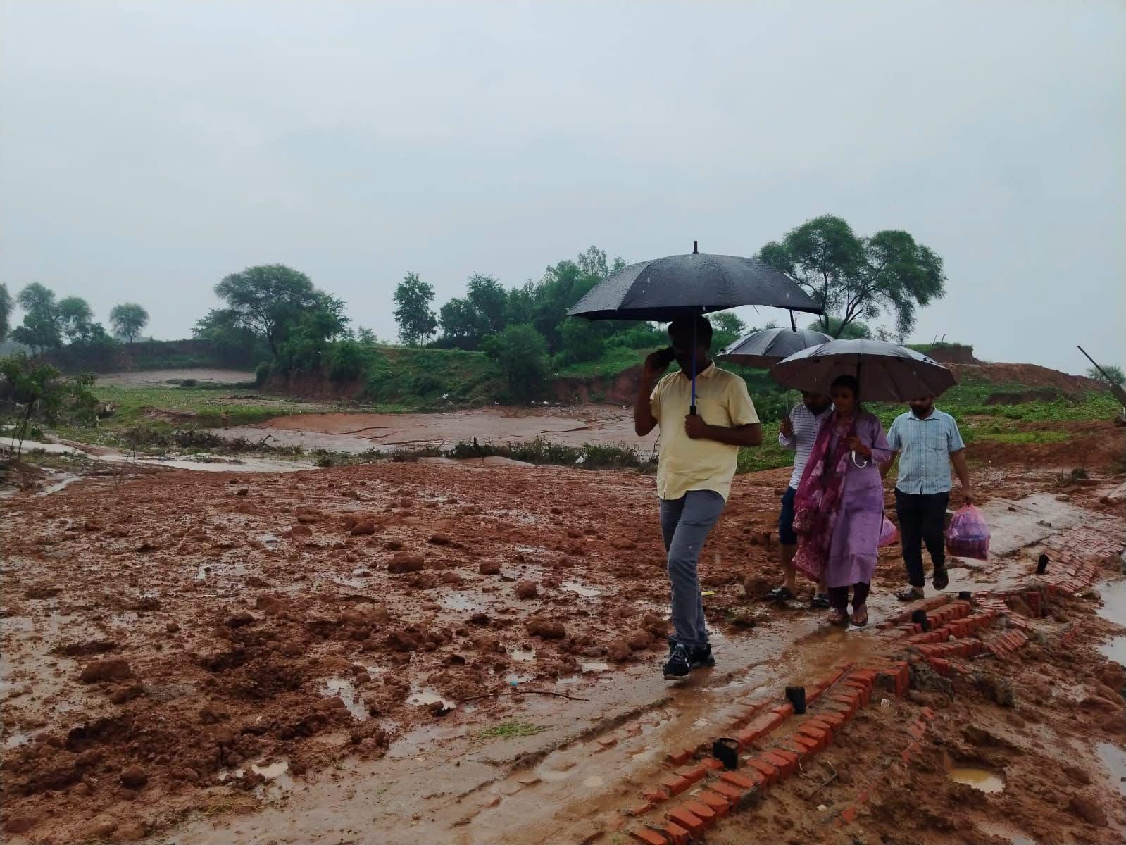 बारिश के बीच छाता लेकर बाढ़ प्रभावित गांव की ओर जाते सतना कलेक्टर और प्रशासनिक टीम
